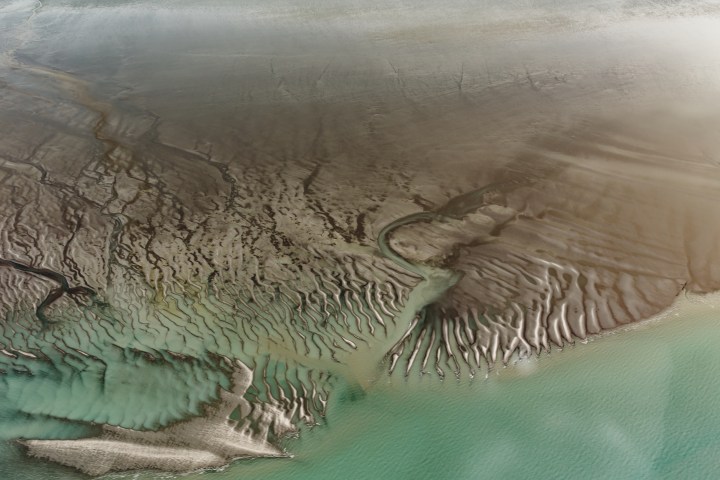 Aerial view of tidal sand patterns meeting turquoise water on a beach.