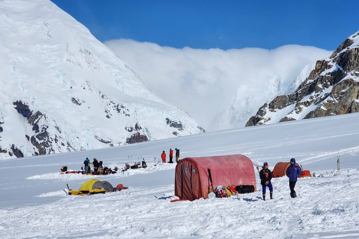 Snowy mountain camp with tents and people in winter gear.