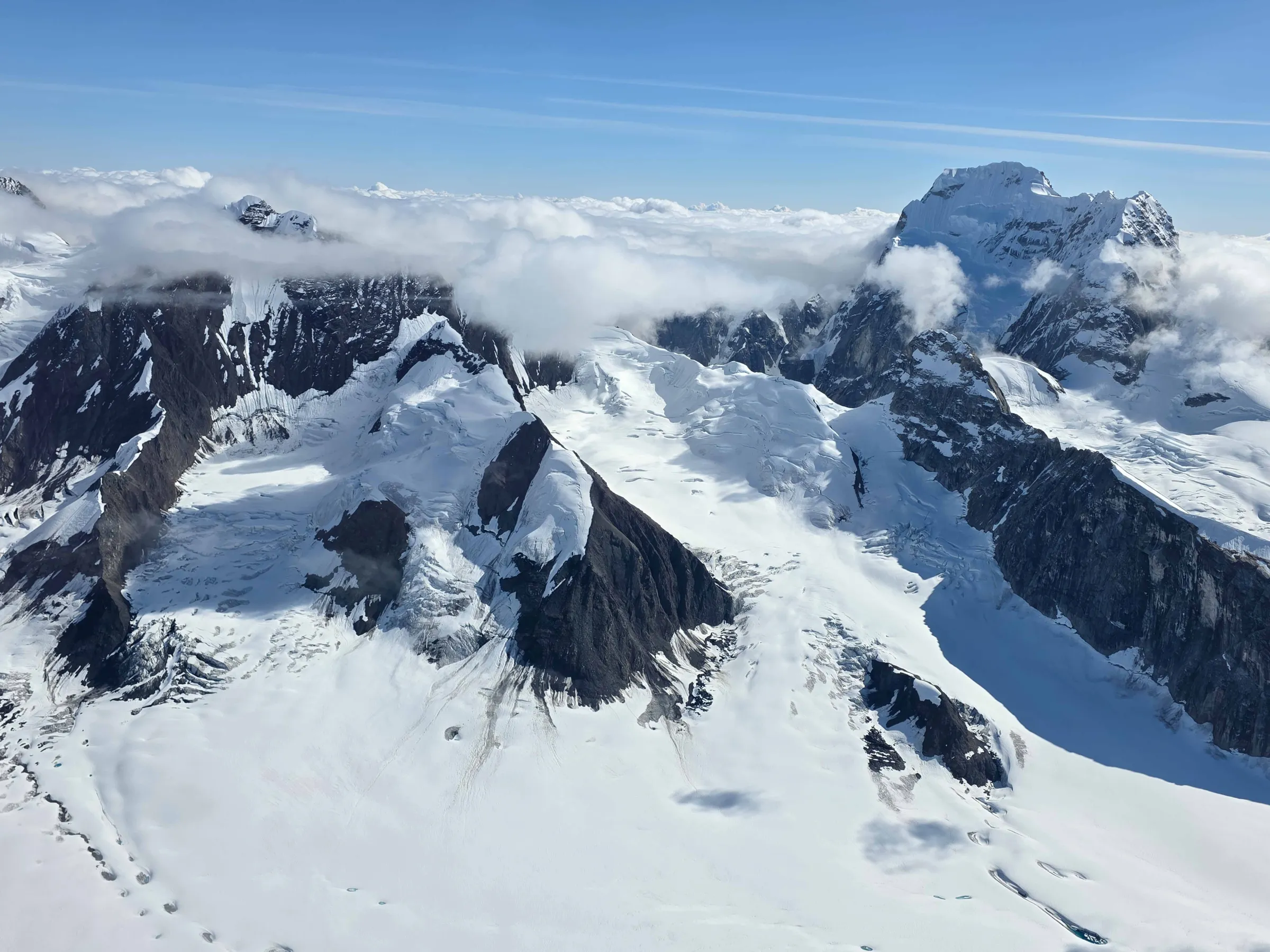 Snow-covered mountain range with scattered clouds and blue sky.