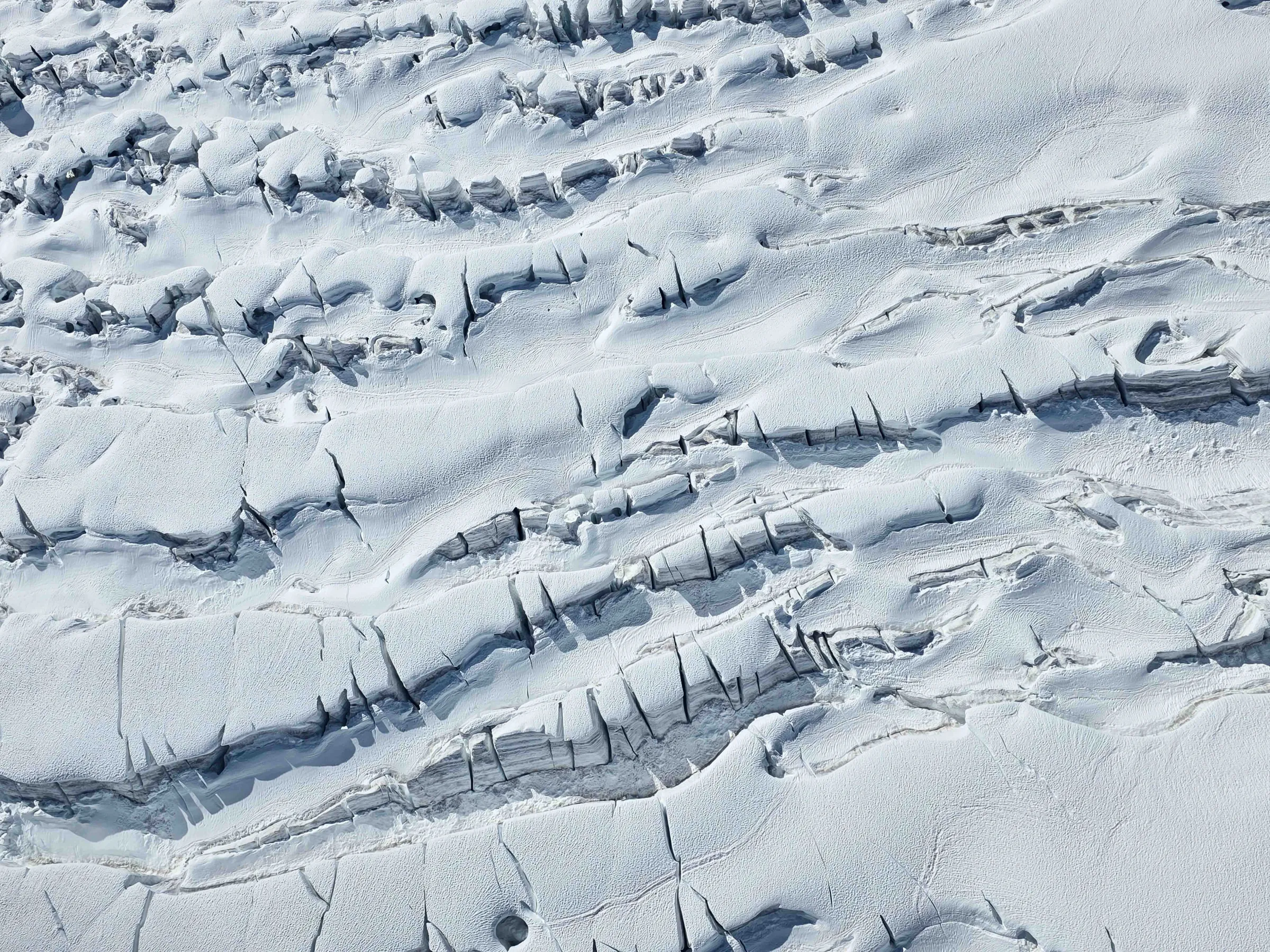 Aerial view of a snow-covered glacier with deep crevasses.