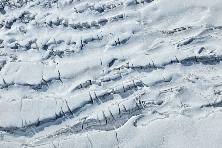 Aerial view of a snow-covered glacier with deep crevasses.