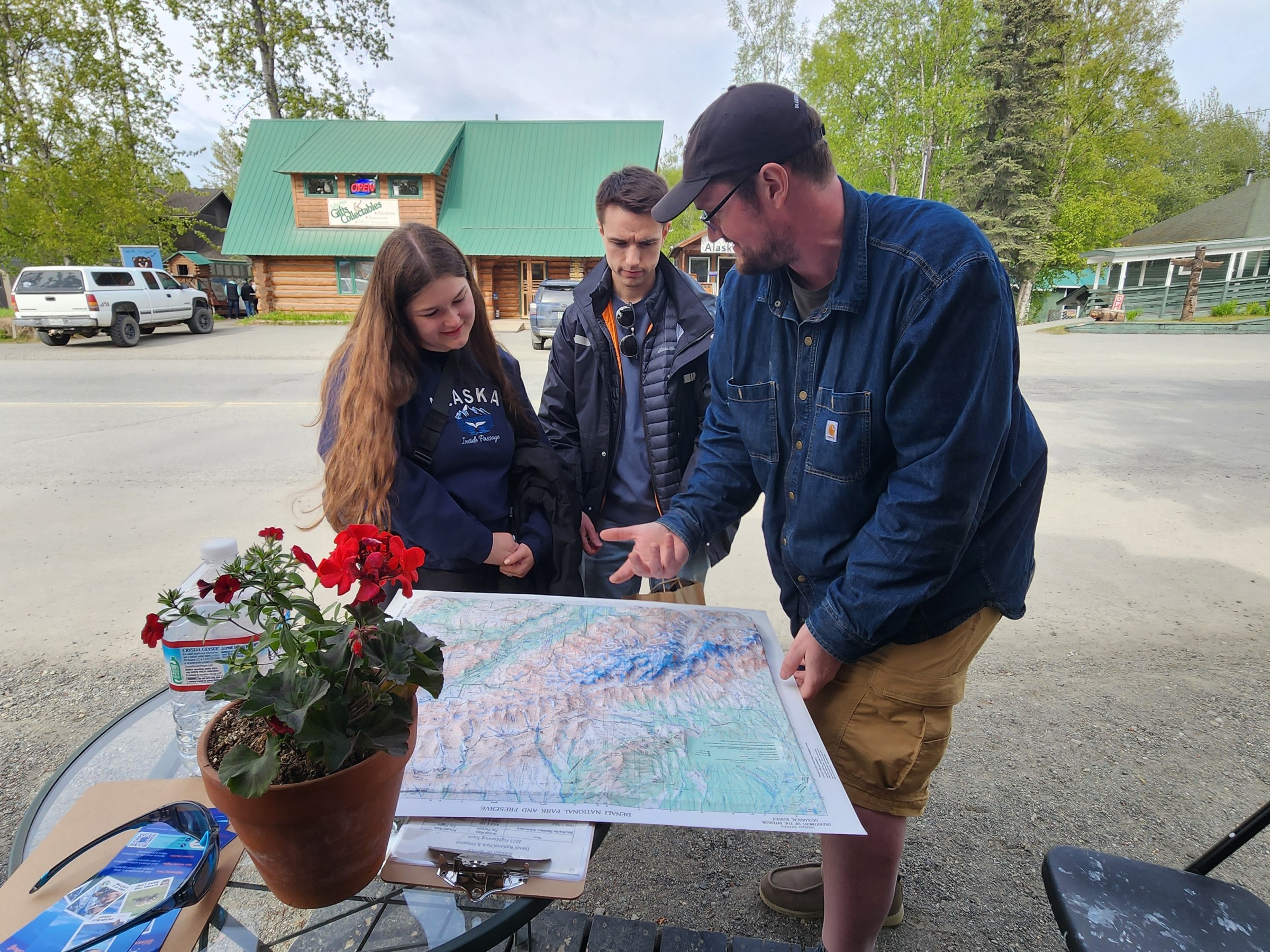 Three people looking at a map on an outdoor table near a road.