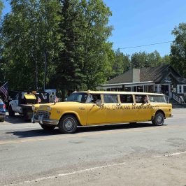Yellow vintage stretch taxi on a street with trees and buildings in the background. 4th July Parade 2025