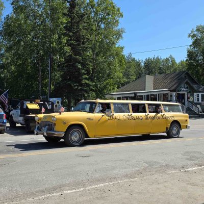 Yellow vintage stretch taxi on a street with trees and buildings in the background. 4th July Parade 2025