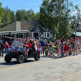 Parade featuring a decorated vehicle and people, including children, walking and carrying a 'Great Alaska Circus' sign Talkeetna Summer 2025