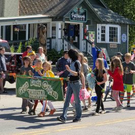 Parade featuring a decorated vehicle and people, including children, walking and carrying a 'Great Alaska Circus' sign Talkeetna Summer 2025