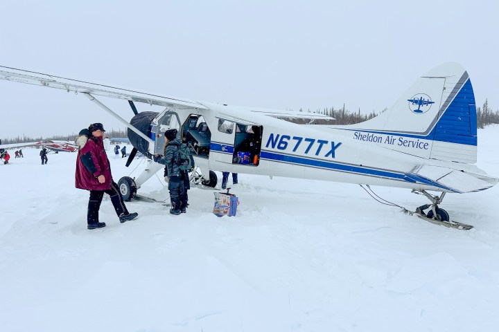 People loading supplies onto small plane in snowy landscape.