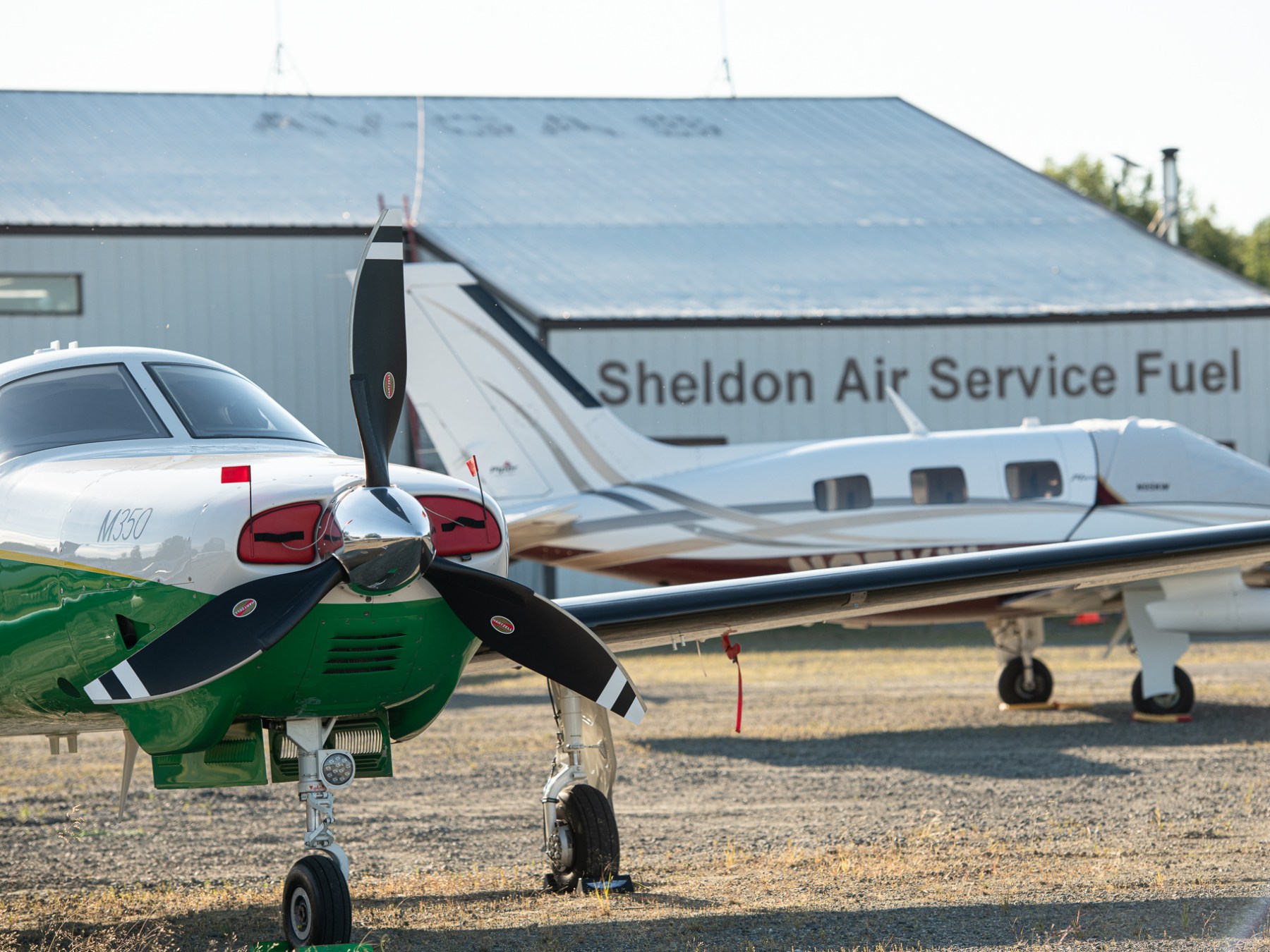 Two small airplanes parked near a hangar labeled 'Sheldon Air Service Fuel.'