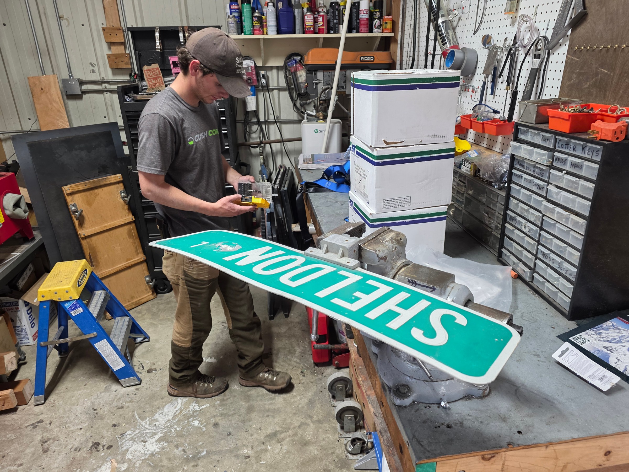 Person in workshop holding package near vise with street sign clamped on workbench.