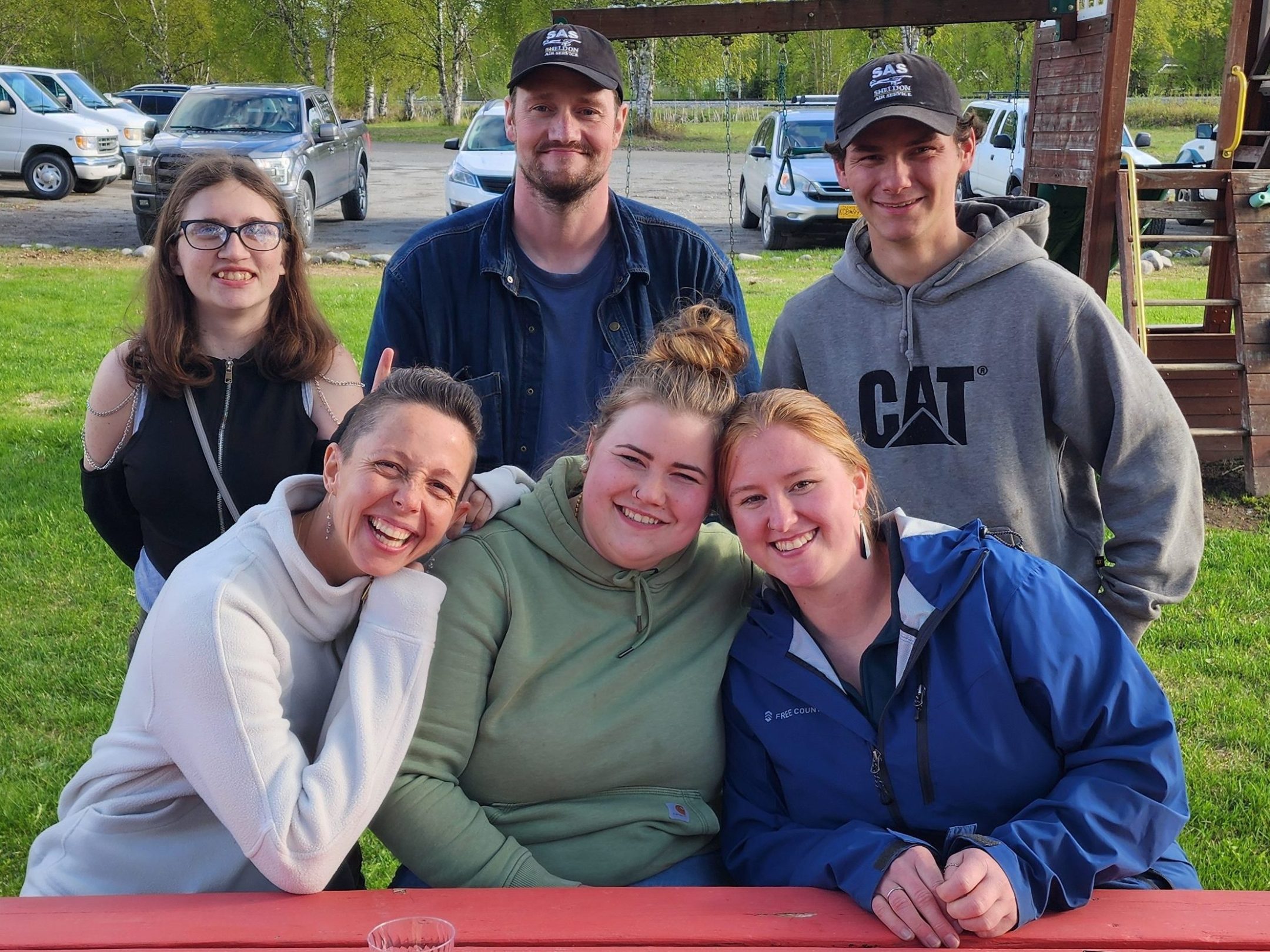 Six people smiling at a picnic table with plates of dessert outdoors.