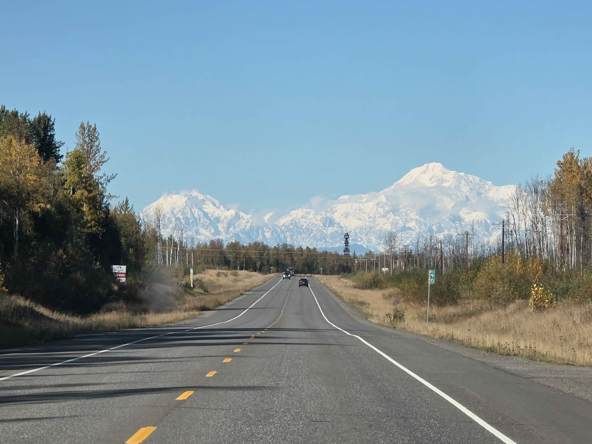 Open road with snowy mountains and trees on a clear day.