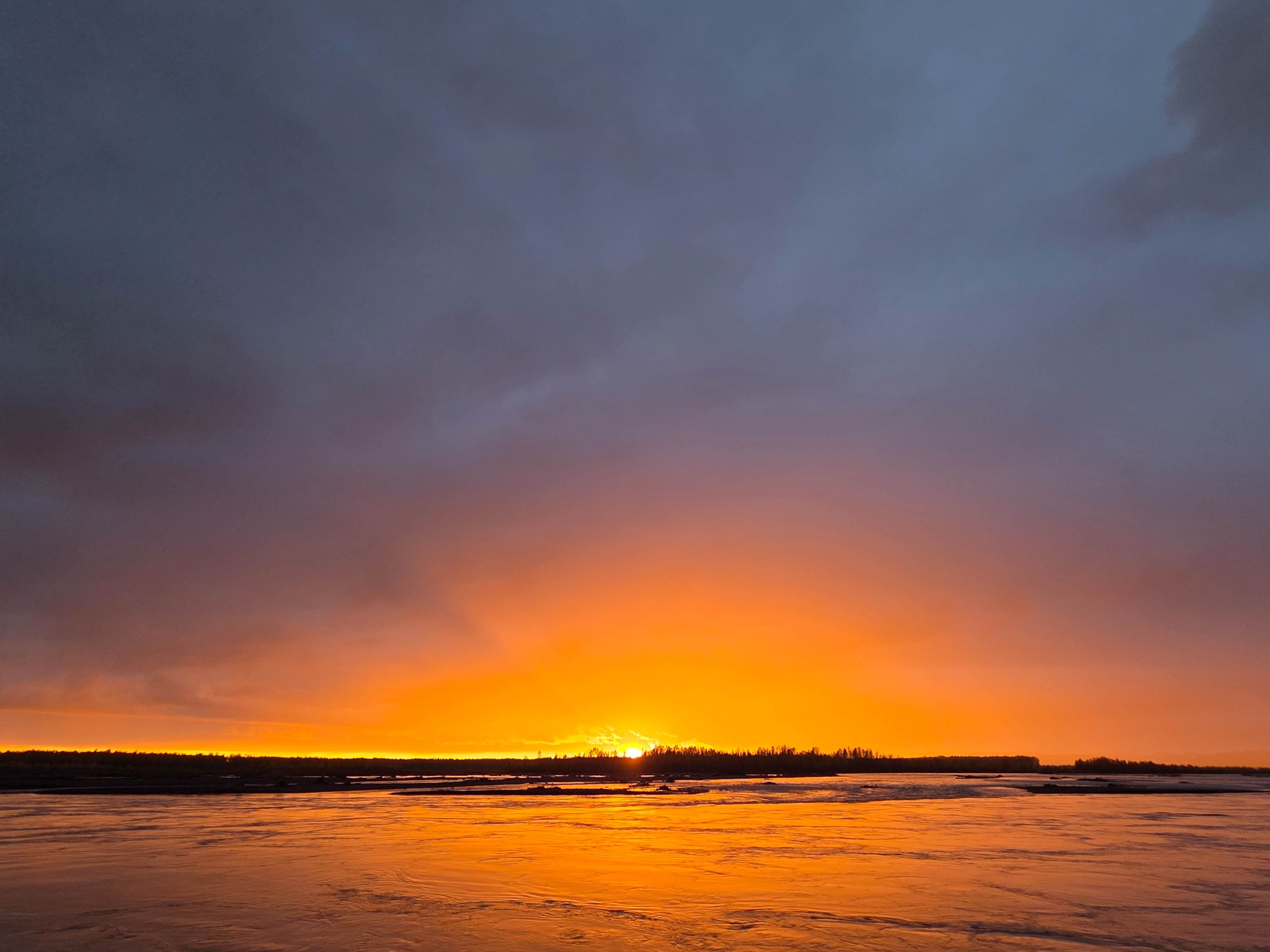 Sunset over a calm lake with an orange glow and dark clouds above.