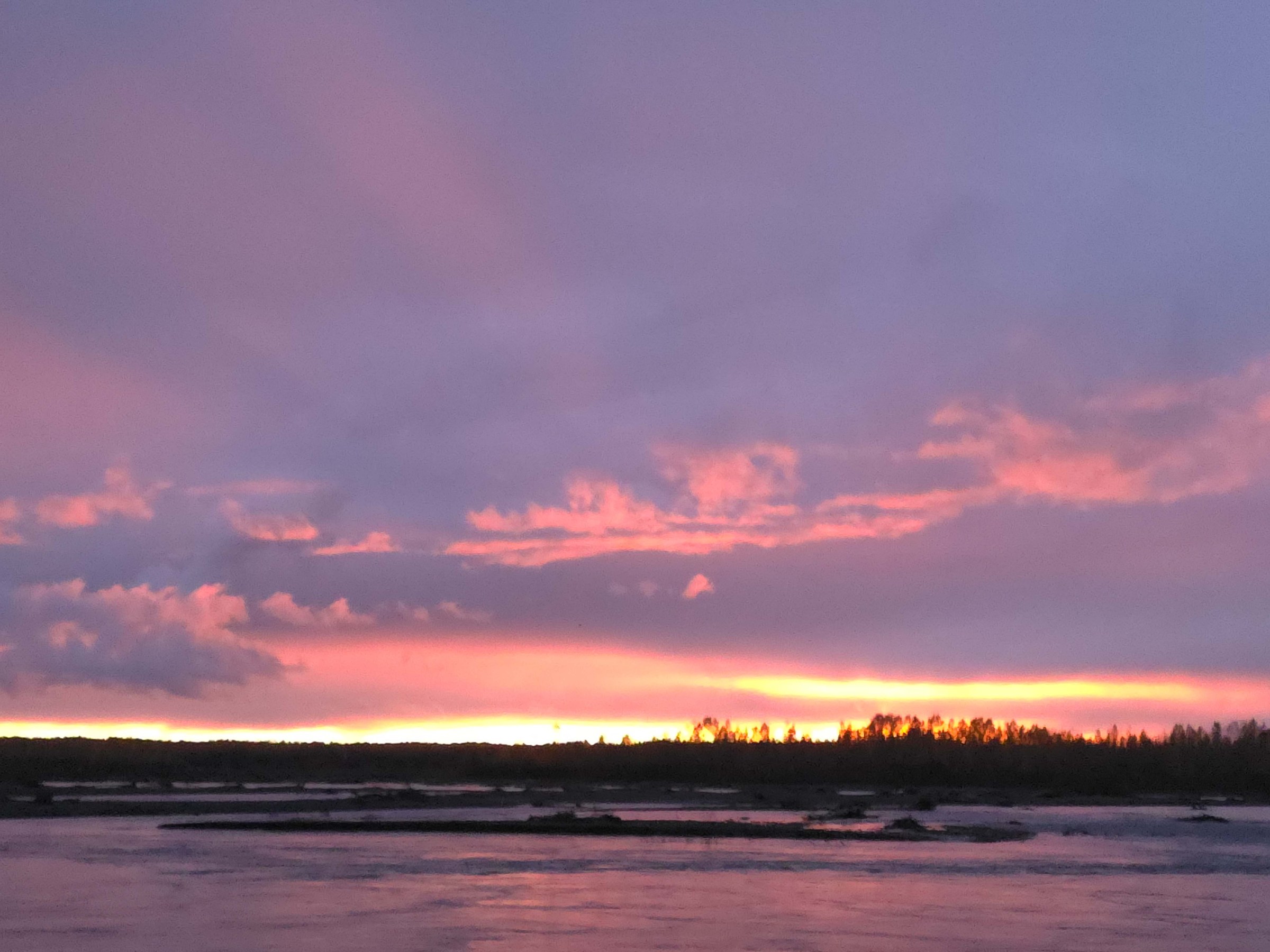 Vibrant sunset over a calm river with pink and purple clouds in the sky.