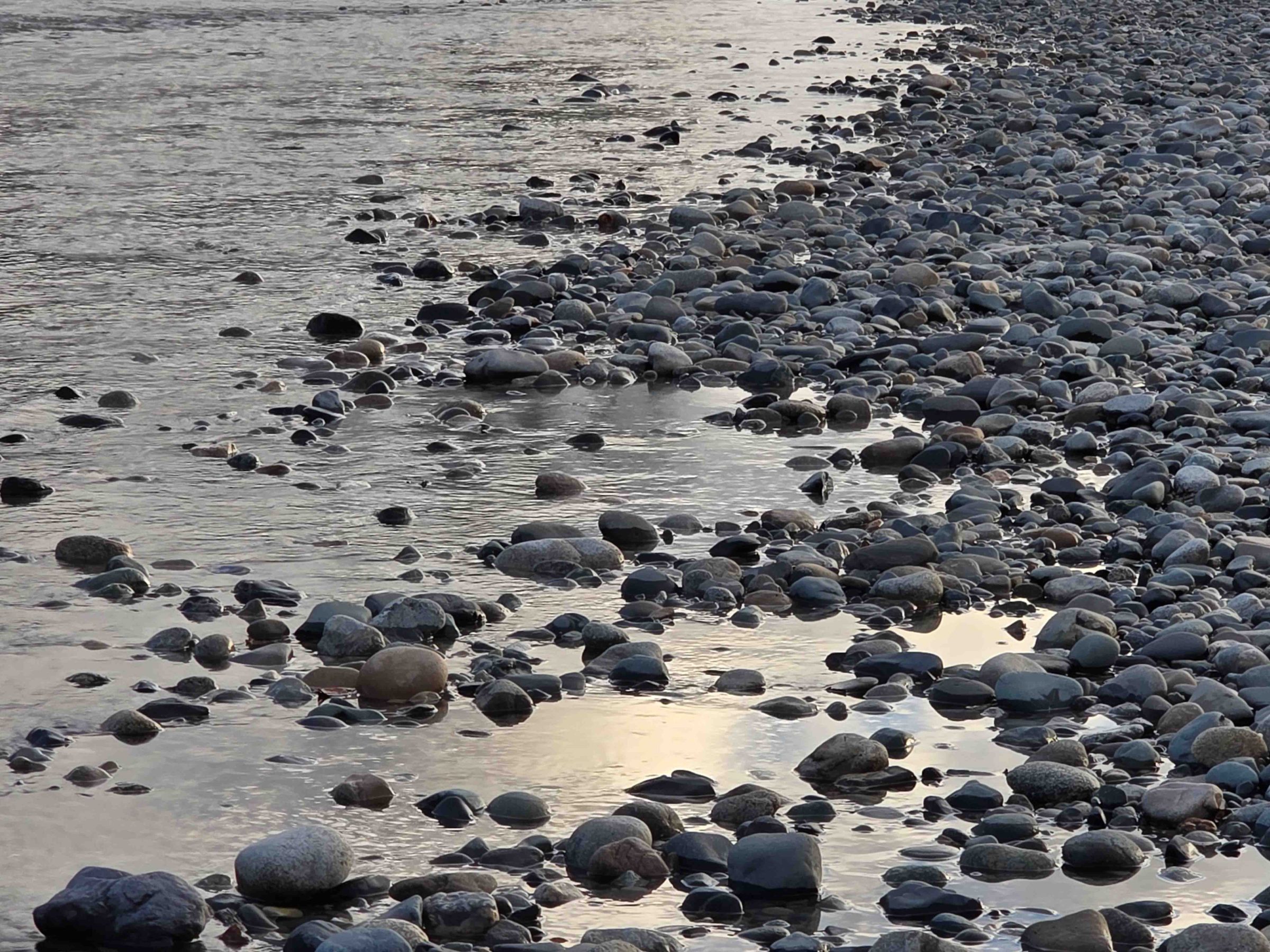 Pebble-covered riverbank with water reflecting sky.