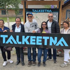 Group of six visitors holding a 'TALKEETNA' sign