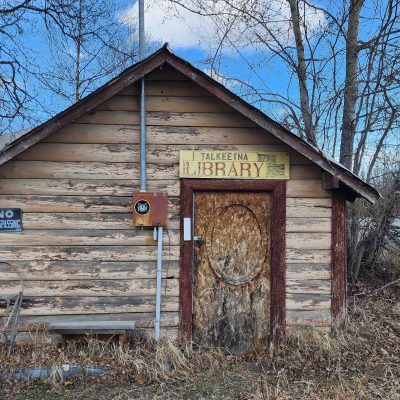 Old wooden building labeled 'Library' with 'No Trespassing' sign and overgrown surroundings.