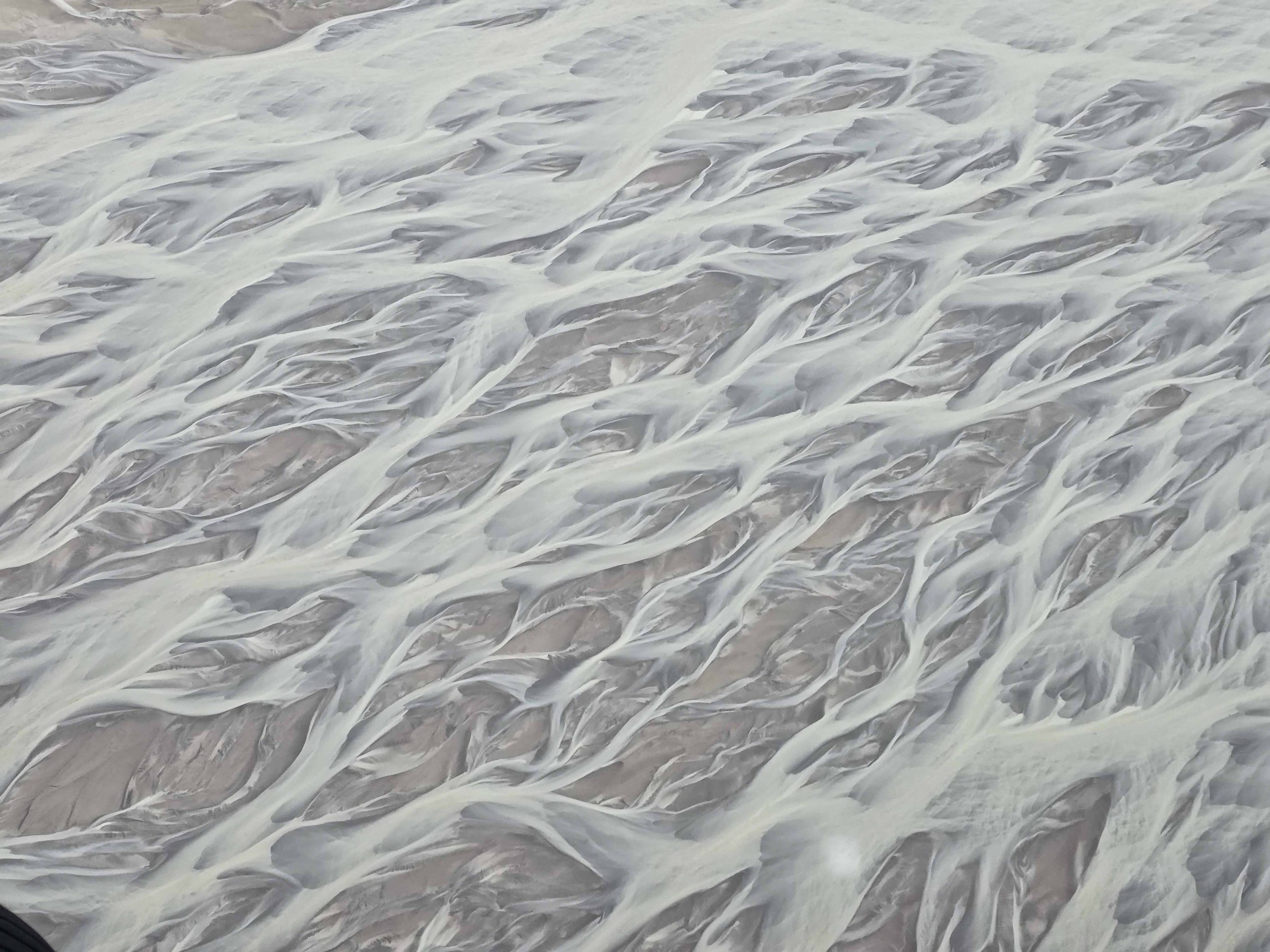 Aerial view of braided river channels with white and grayish tones.