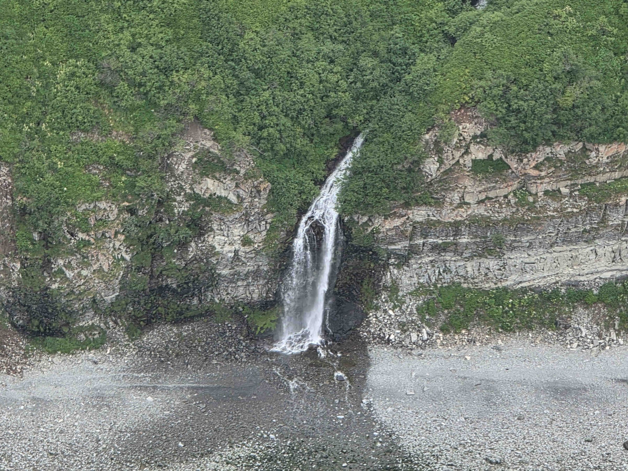 Waterfall cascading down a cliff surrounded by lush greenery and rocks.