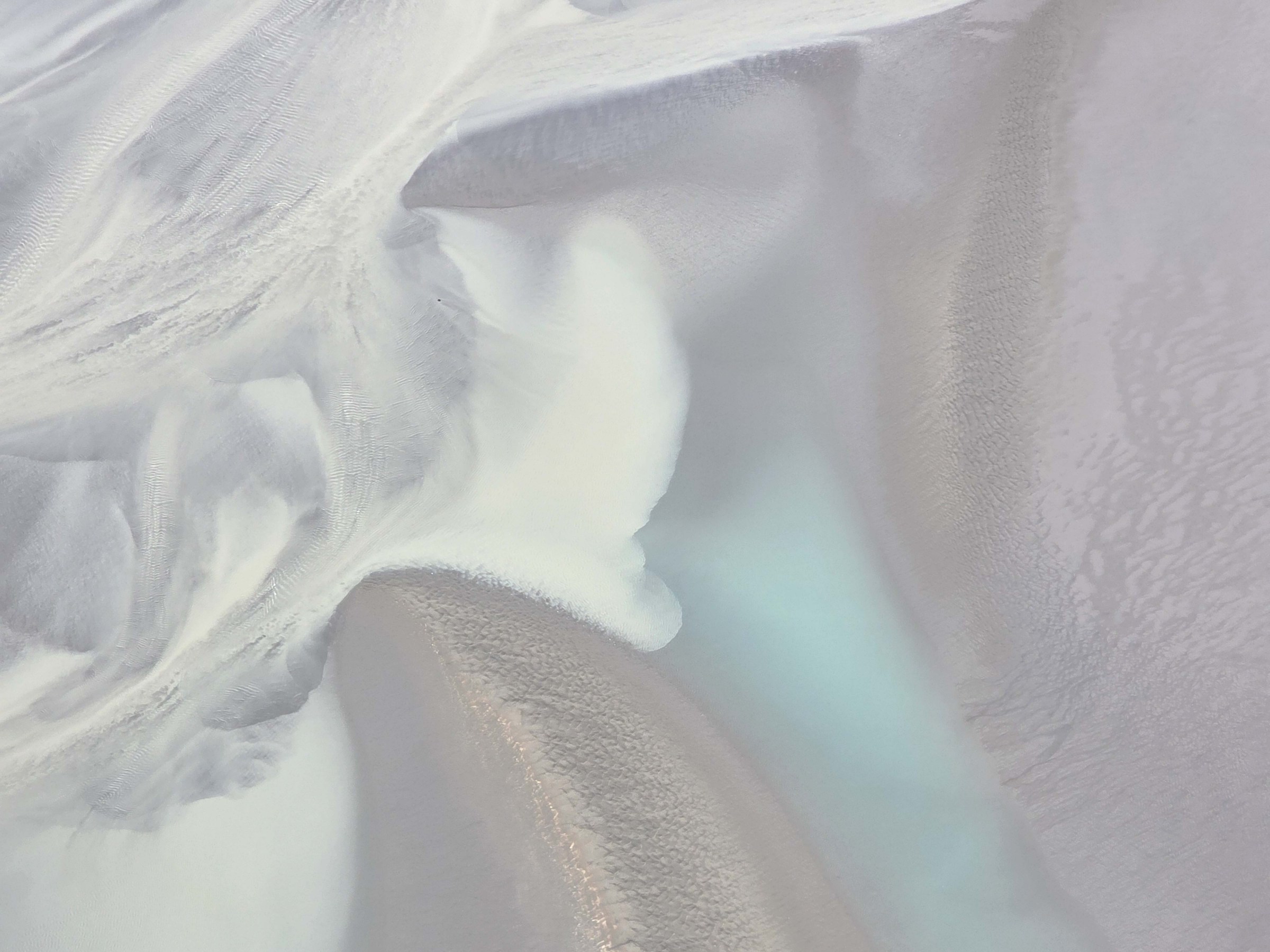 Abstract aerial view of a river delta with swirling sand patterns and turquoise water.