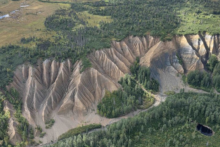 Aerial view of eroded cliffs with rugged terrain and dense forest in the background.
