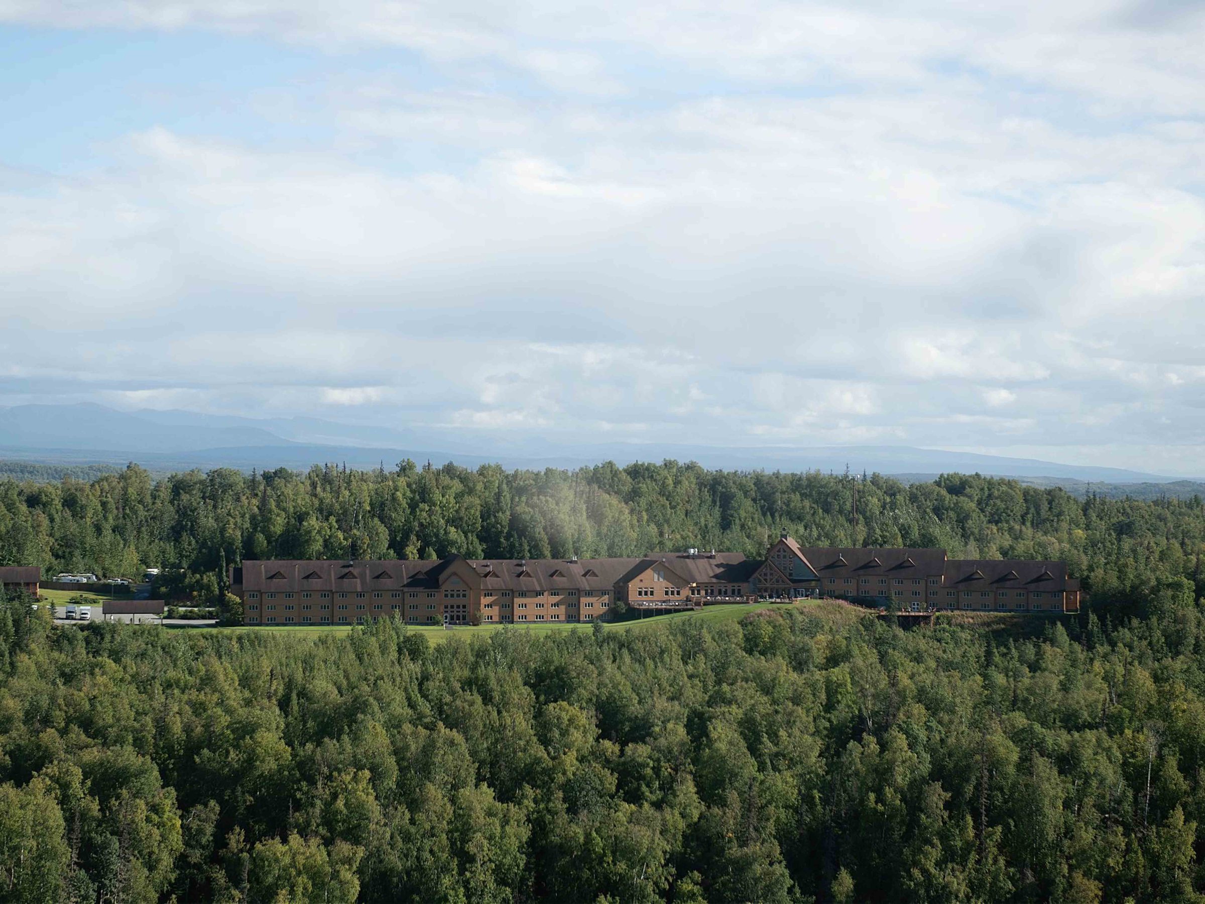 A large lodge surrounded by dense forest under a cloudy sky.