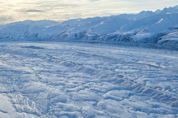 Snow-covered mountain range with textured glacier under a cloudy sky.