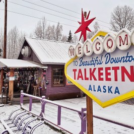 Sign reading 'Welcome to Beautiful Downtown Talkeetna, Alaska' in snowy town with trees in Talkeetna Alaska