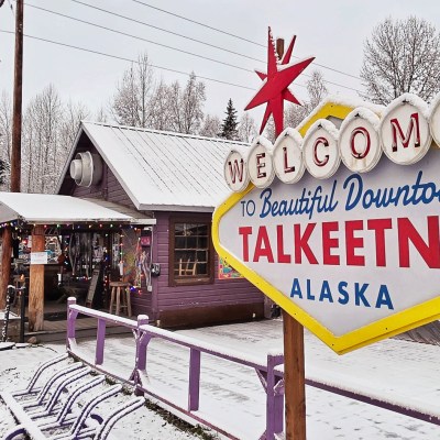 Sign reading 'Welcome to Beautiful Downtown Talkeetna, Alaska' in snowy town with trees in Talkeetna Alaska