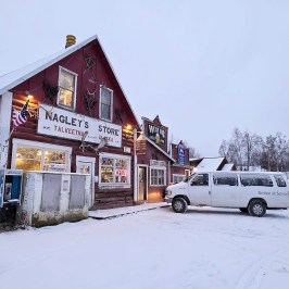 Red wooden store Nagleys in snowy landscape, white van parked outside, winter wonderland