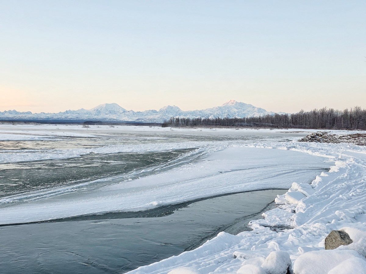 Snow-covered landscape with frozen river and Denali on the distance at sunrise.