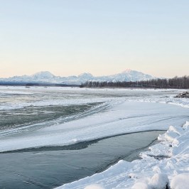 Snow-covered landscape with frozen river and Denali on the distance at sunrise.