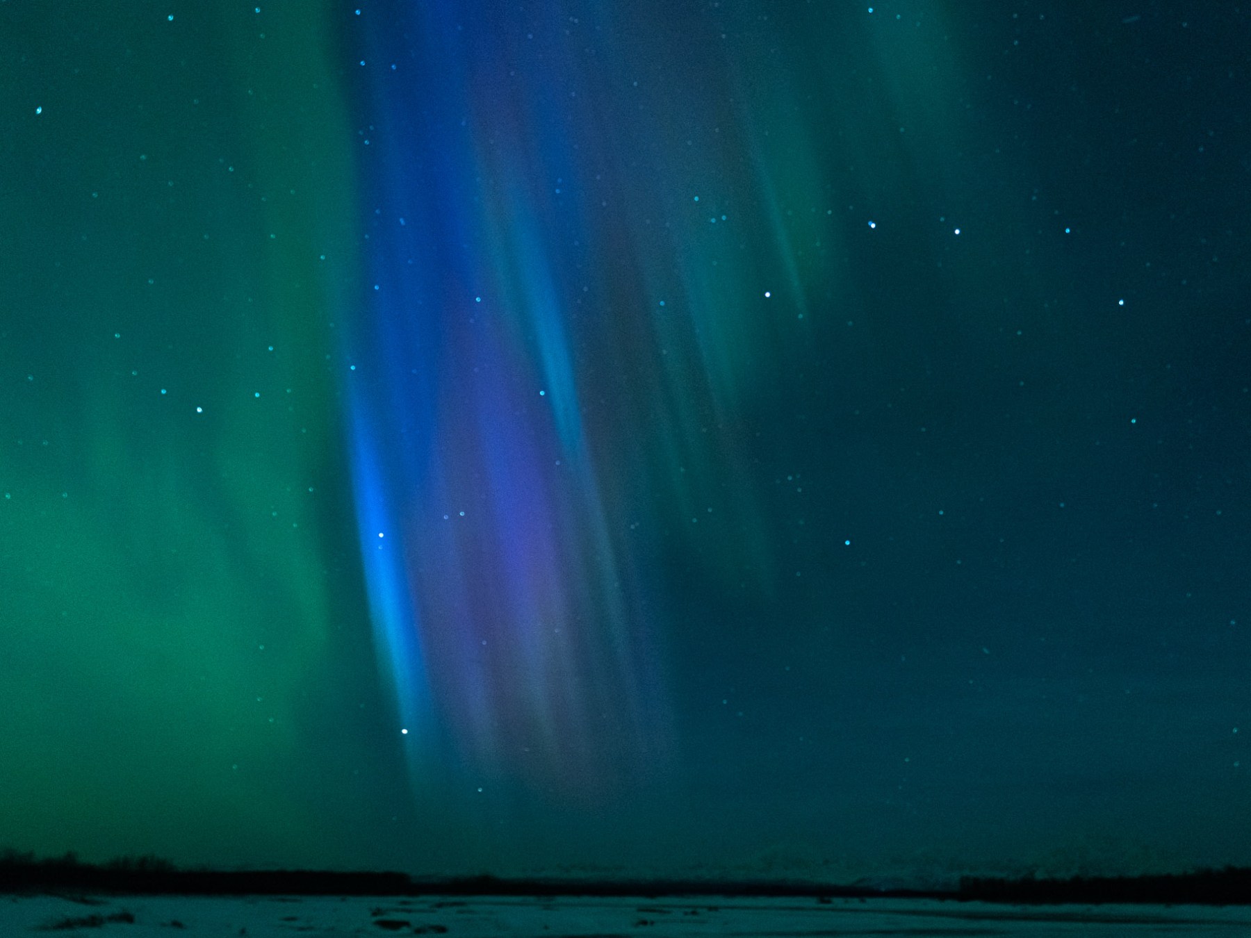 Aurora borealis with green and purple lights in night sky over snowy landscape.