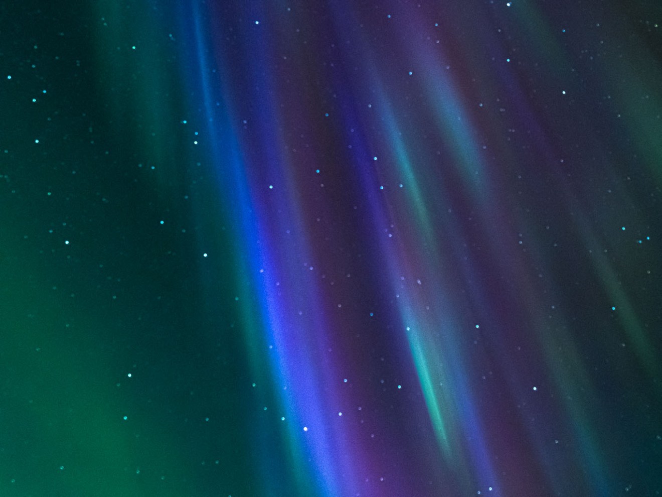 Vibrant aurora borealis with green, blue, and purple hues and scattered stars in the night sky.