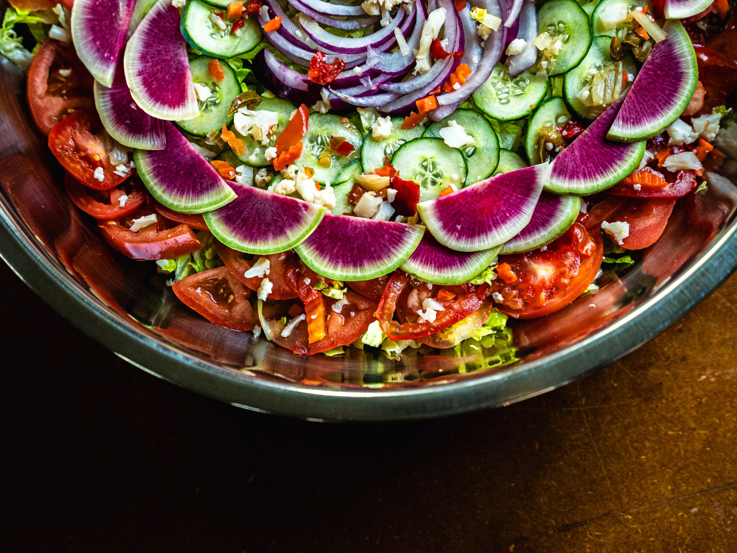 Colorful salad with radishes, cucumbers, tomatoes, and red onion in a metal bowl.