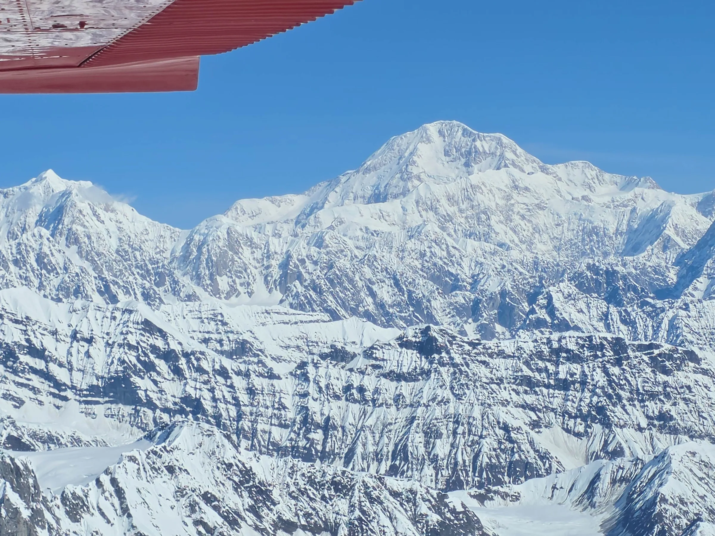Snow-covered mountains viewed from an airplane with a red wing.