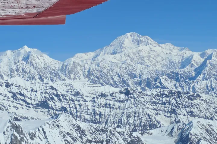 Snow-covered mountains viewed from an airplane with a red wing.