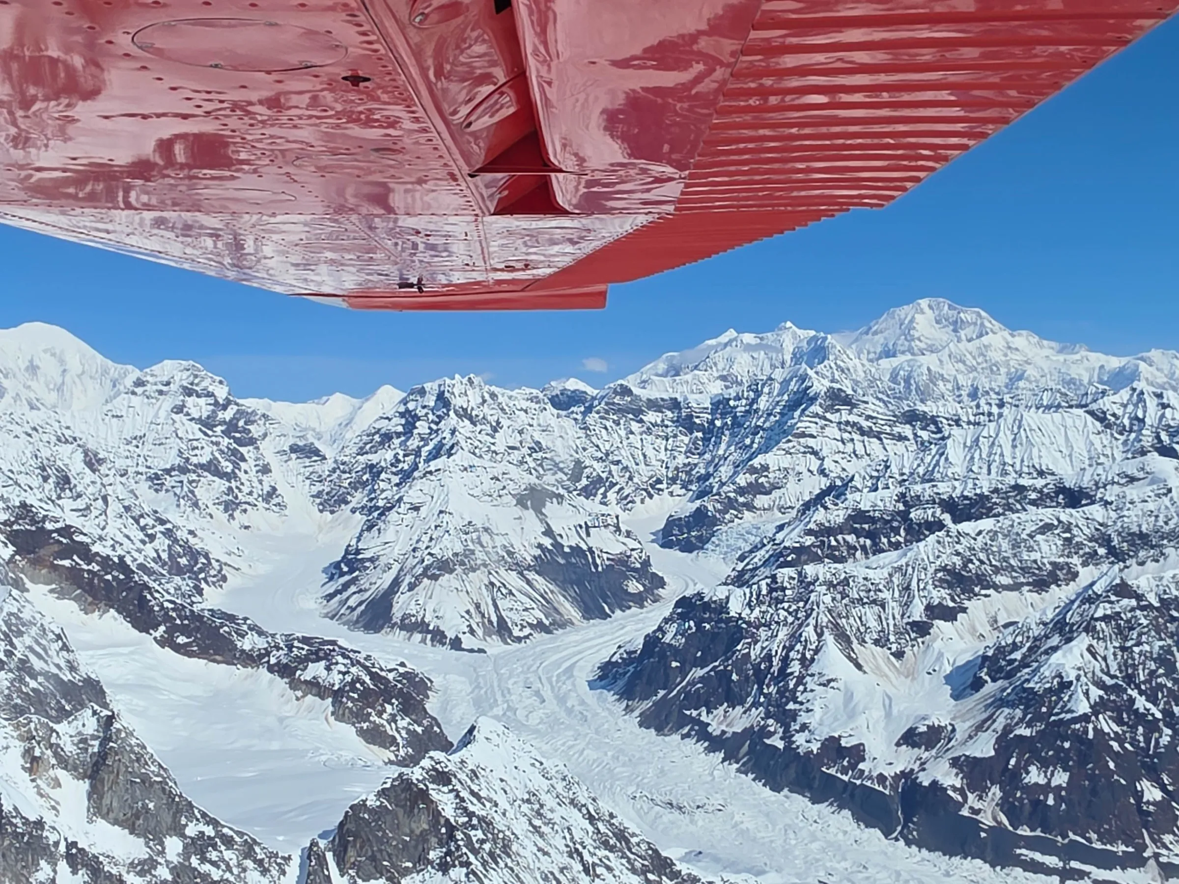 Snowy mountain landscape viewed from an airplane window under red wing.