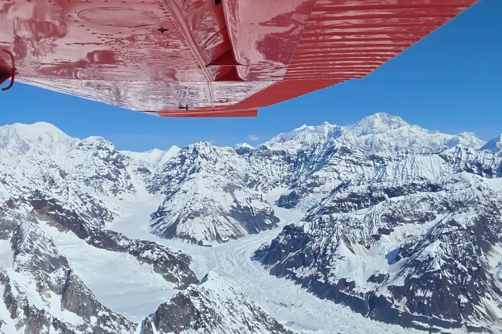 Snowy mountain landscape viewed from an airplane window under red wing.