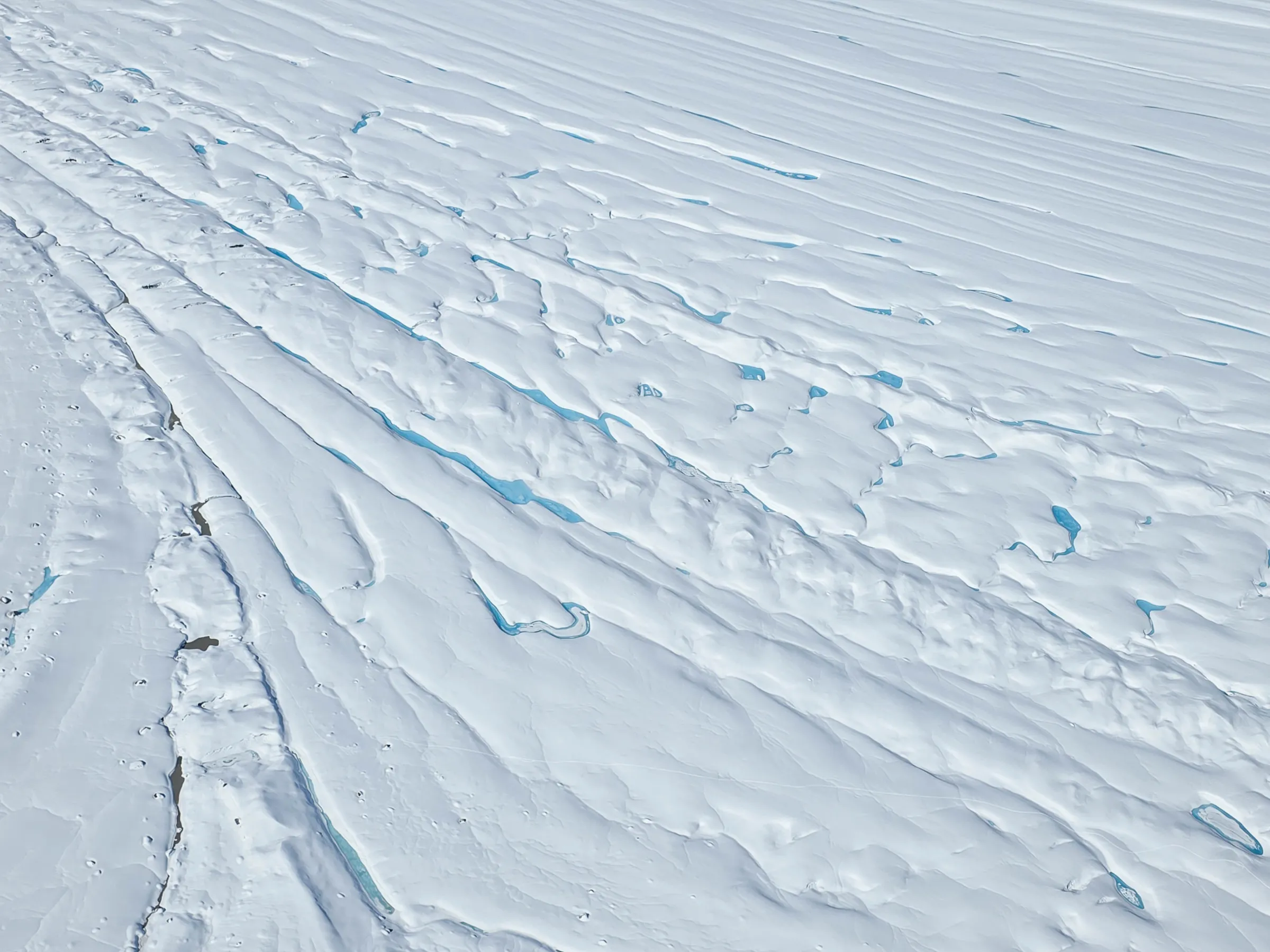 Aerial view of an expansive snowy glacier with visible blue ice cracks and ridges.