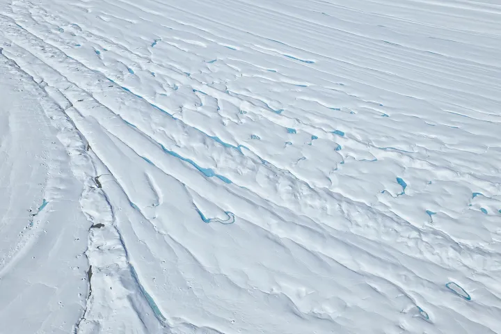 Aerial view of an expansive snowy glacier with visible blue ice cracks and ridges.