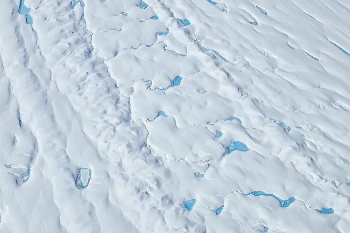 Aerial view of snowy landscape with scattered blue melt ponds.