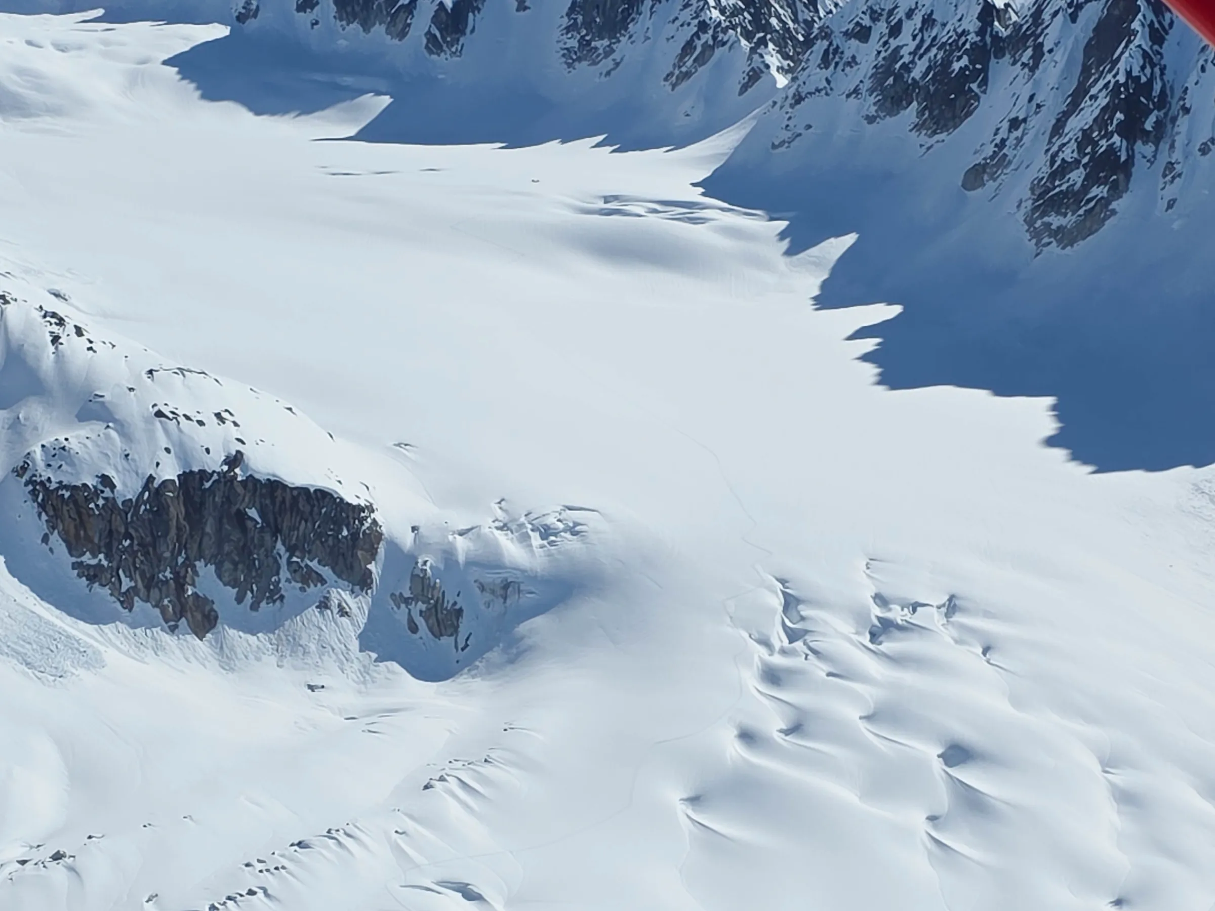 Aerial view of snowy mountains and glacier under clear blue sky.