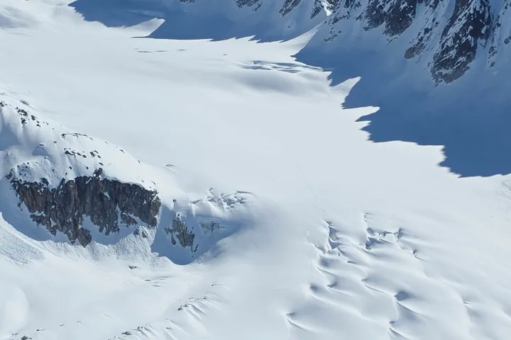 Aerial view of snowy mountains and glacier under clear blue sky.