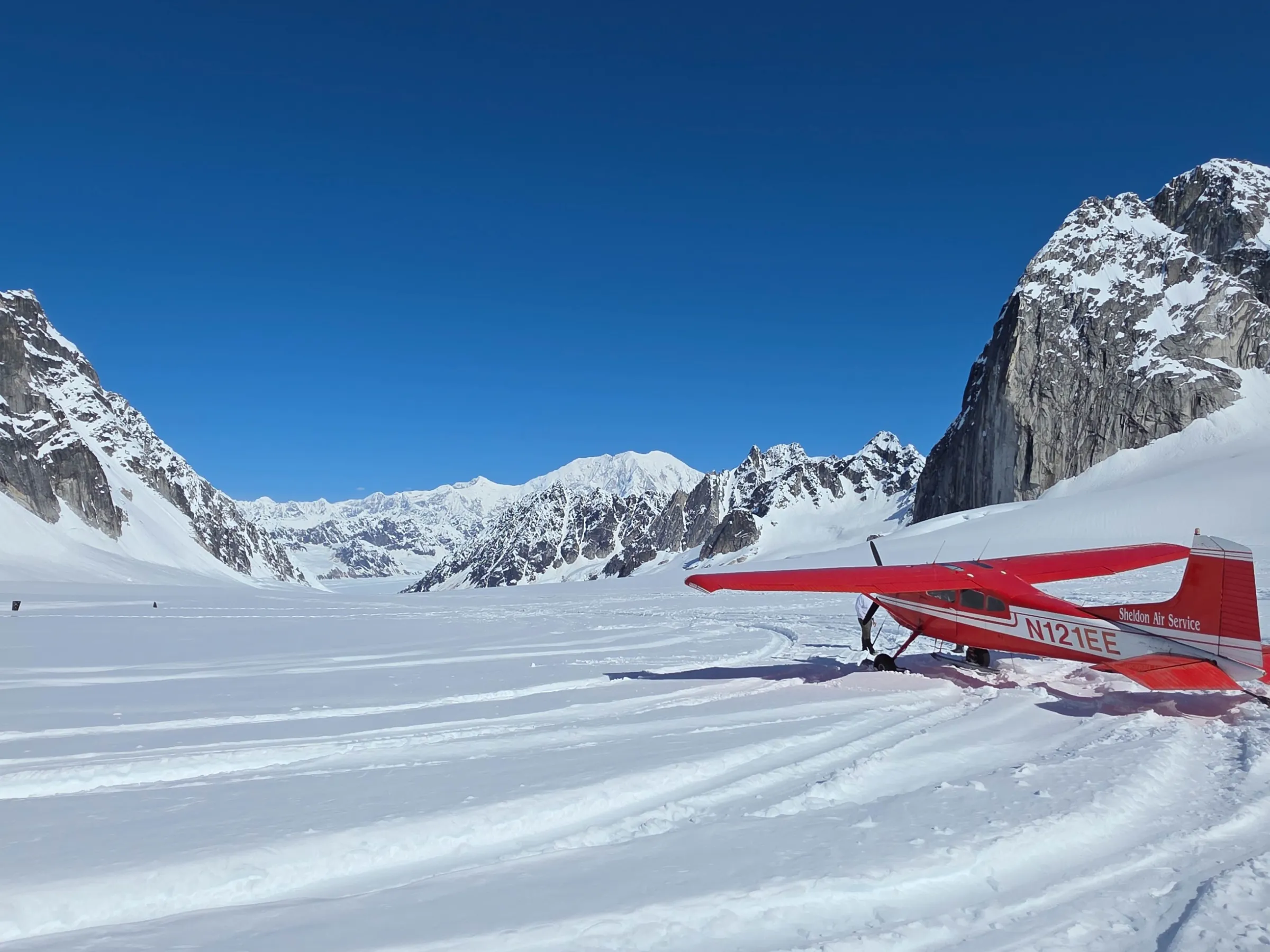 Red ski plane on a snowy mountain landscape under clear blue sky.