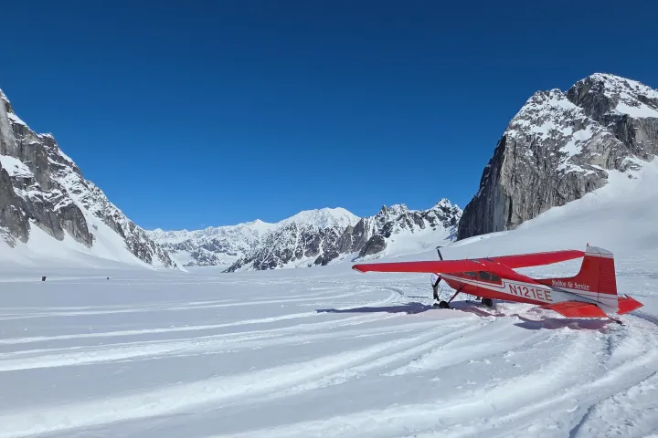 Red ski plane on a snowy mountain landscape under clear blue sky.