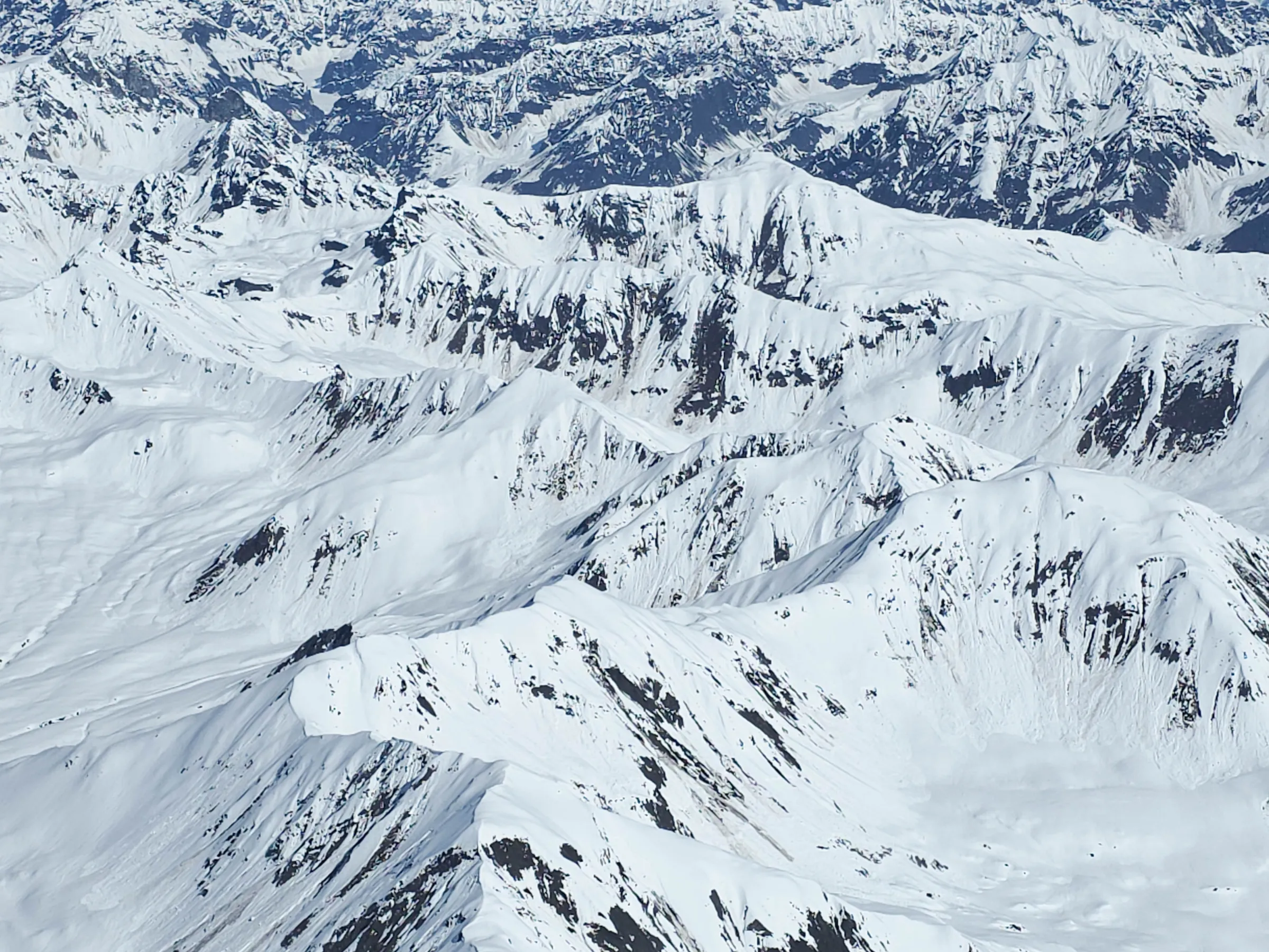Aerial view of snowy mountain range under a clear blue sky.
