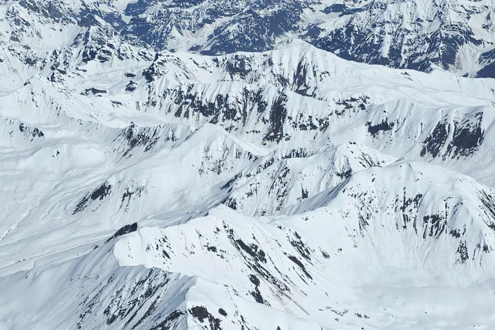Aerial view of snowy mountain range under a clear blue sky.