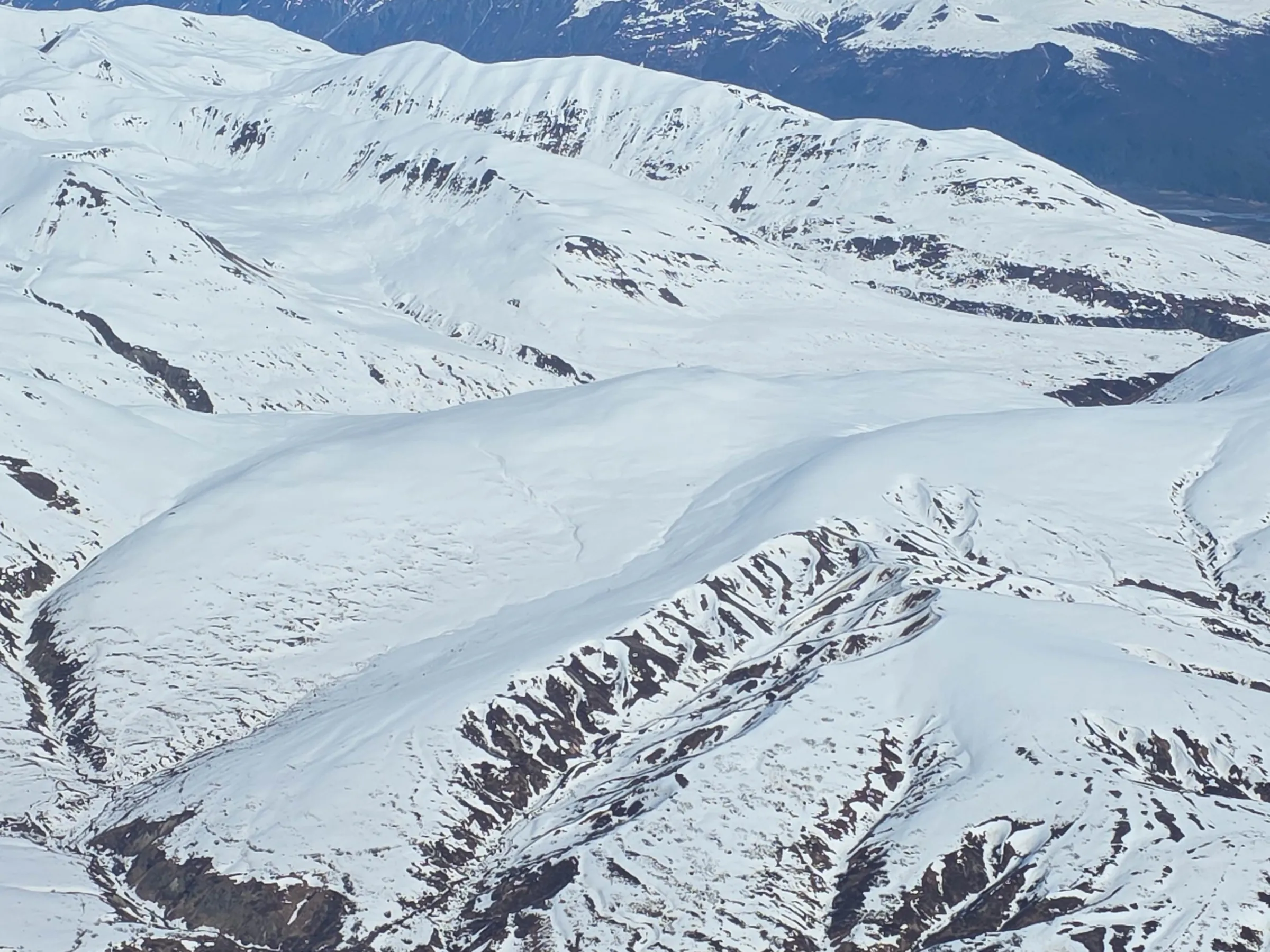 Snow-covered mountains and valleys under clear blue sky.