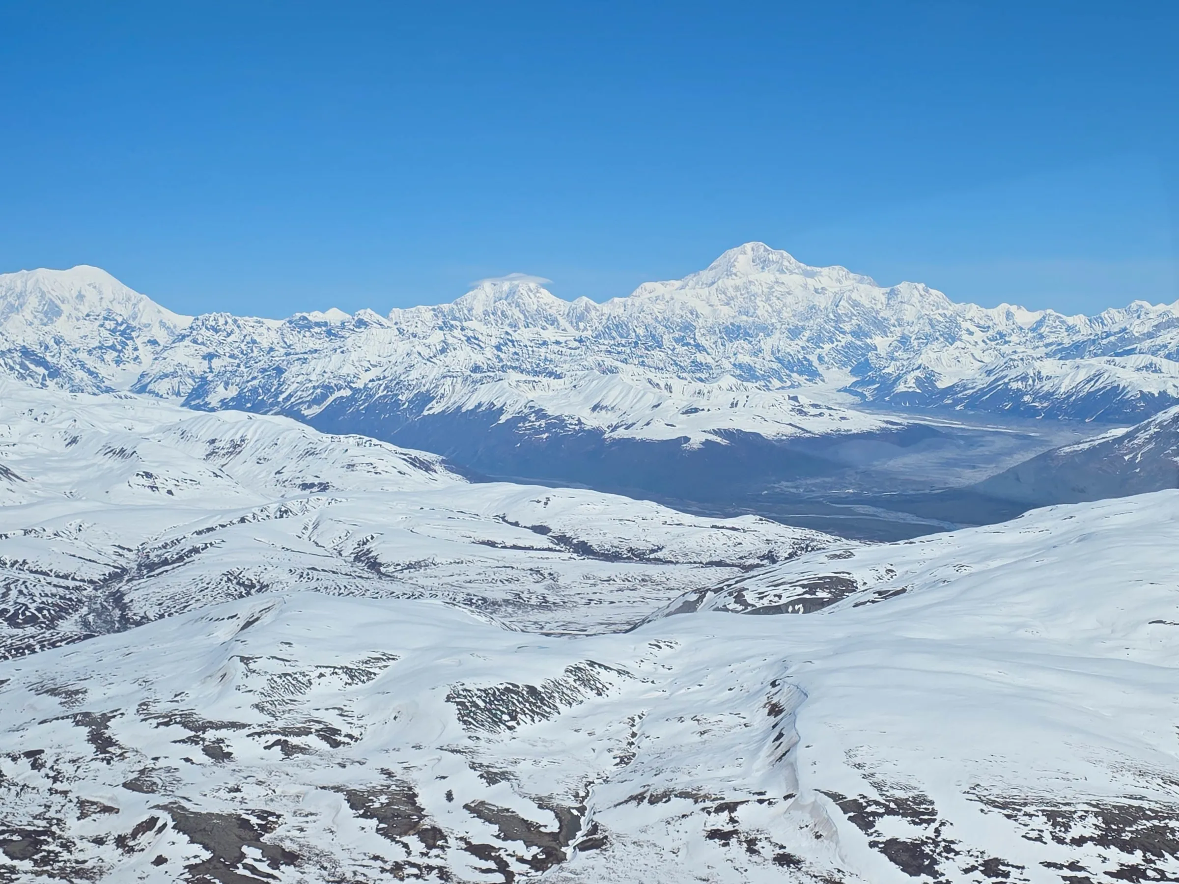 Aerial view of snowy mountains under a clear blue sky.