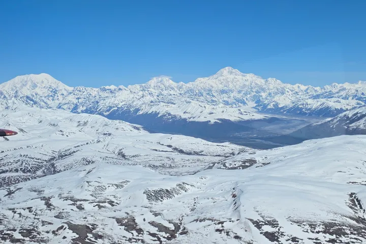 Aerial view of snowy mountains under a clear blue sky.
